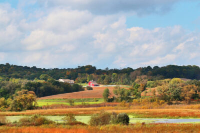 Autumn rural landscape with houses scattered among forested hills and fields and blue cloudy sky over. Typical Wisconsin countryside view, Midwest USA.