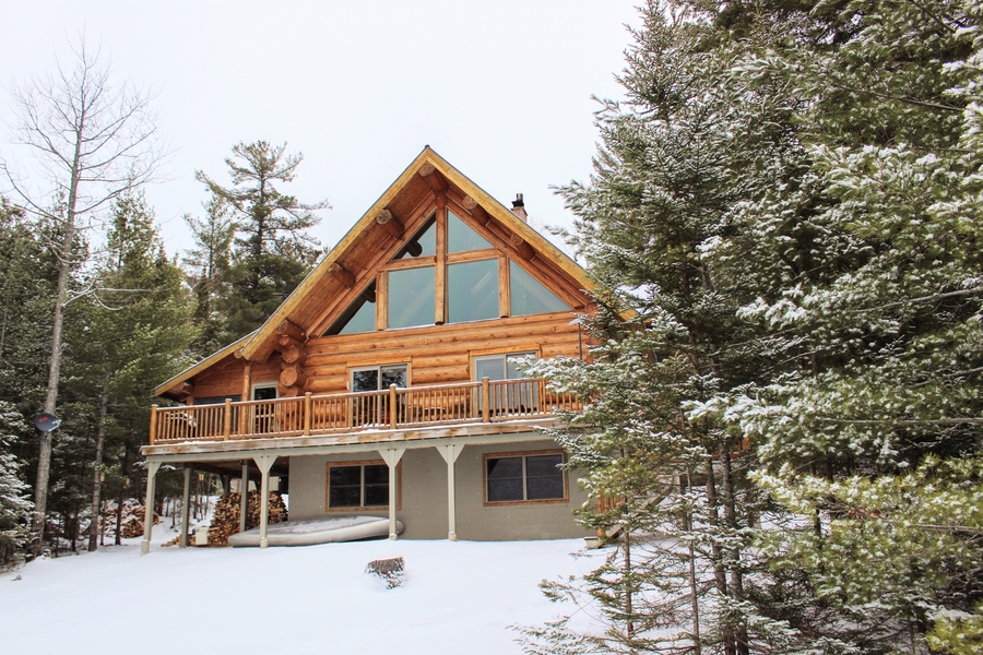 Custom Log Home with snow on the ground, large trees in the foreground and background.